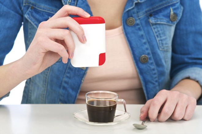 Женщина кладет подсластитель в кофе