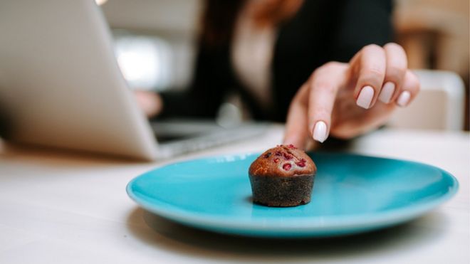 Una mujer frente a una computadora toma un pastel.