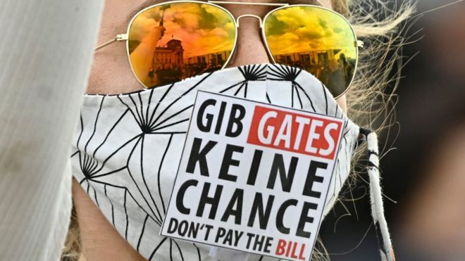 A protester wears a mask which says in German and English: "GIB GATES KEINE CHANCE DON'T PAY THE BILL"