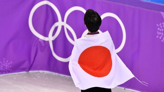 Un atleta japonés de espaldas envuelto en la bandera del país frente a los anillos de los Juegos Olímpicos.