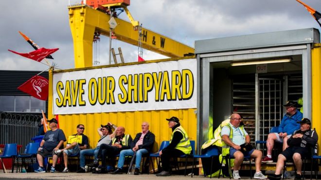 Сотрудники Harland and Wolff во время акции протеста у ворот верфи в Белфасте, ожидая услышать, будет ли заключена последняя сделка, чтобы не допустить закрытия бизнеса,