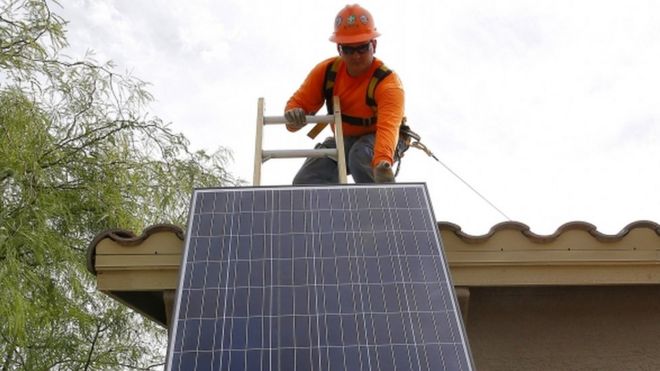 Работник, устанавливающий солнечную батарею на крыше