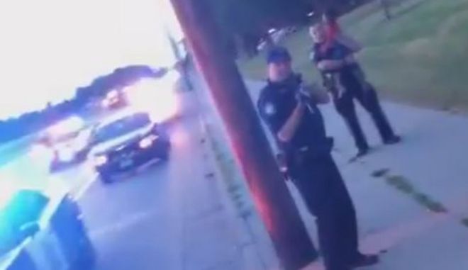 Кадр из Facebook Live показывает, что полицейская машина и полицейский рядом с ней направляют пистолет на женщину - за ним стоит еще один полицейский с молодой девушкой - июль 2016 г.