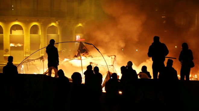 Protesters stand near burning tents during anti government protests in Beirut