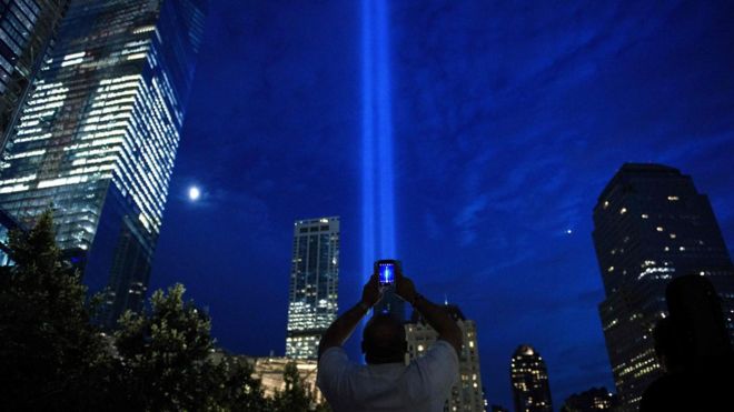 Мужчина фотографирует лучи света, символизирующие две башни Всемирного торгового центра в ночь перед 15-й годовщиной терактов 11 сентября 2001 года в Соединенных Штатах