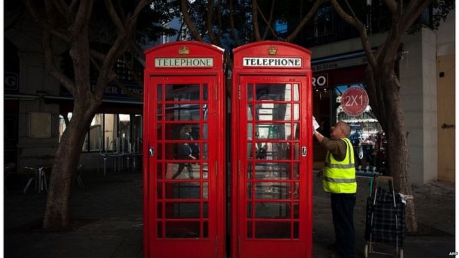 Un hombre limpia una caseta telefónica en la calle en Gibraltar.