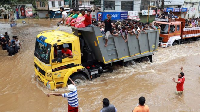 Индийские пассажиры едут на грузовике в более безопасное место, так как паводковые воды разрушают Национальное шоссе 47 в районе Эрнакулам города Кочи