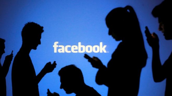 Силуэты фигуры стоят перед логотипом Facebook