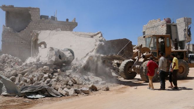 Бульдозер убирает обломки здания, разрушенного правительственной бомбардировкой, в удерживаемом повстанцами городе Урум-эль-Кубра, Сирия (11 августа 2018 года)