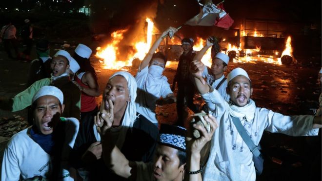 Мусульманские протестующие выкрикивают лозунги возле горящих полицейских грузовиков во время столкновения с полицией возле президентского дворца в Джакарте, Индонезия, в пятницу, 4 ноября 2016 года.