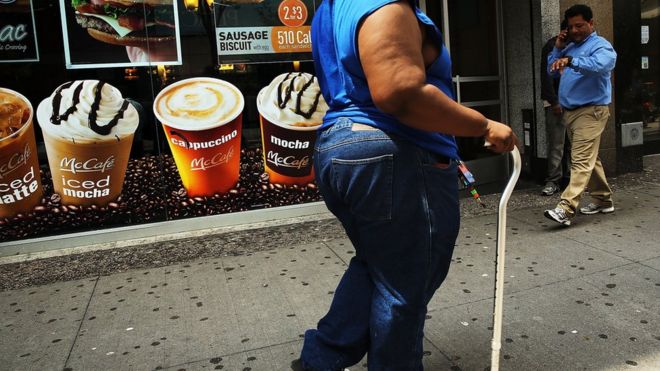 Человек с избыточным весом проходит мимо знака рекламы сладких напитков