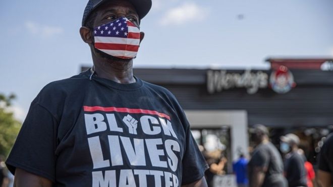 Протестующий стоит у ресторана Венди, который был подожжен после того, как в пятницу, 14 июня 2020 года, полицейский выстрелил в чернокожего мужчину