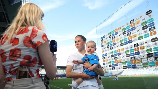 Sara Björk Gunnarsdóttir holds her baby while speaking to a reporter on the pitch