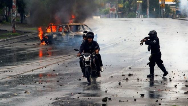 Сотрудник ОМОНа стреляет из своего ружья в отношении двух мужчин во время акции протеста против правительства президента Никарагуа Даниэля Ортеги в Манагуа, Никарагуа, 28 мая