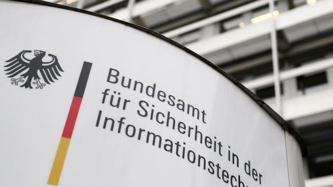 Надпись на немецком языке, на которой изображены цвета немецкого флага и федерального символа, стоит перед большим белым зданием