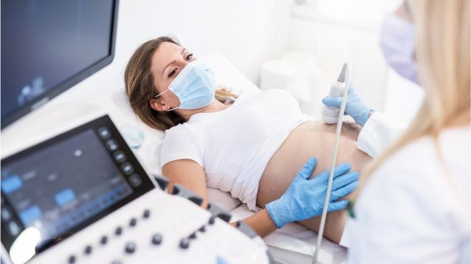 беременная женщина в хирургической маске и перчатках проходит УЗИ