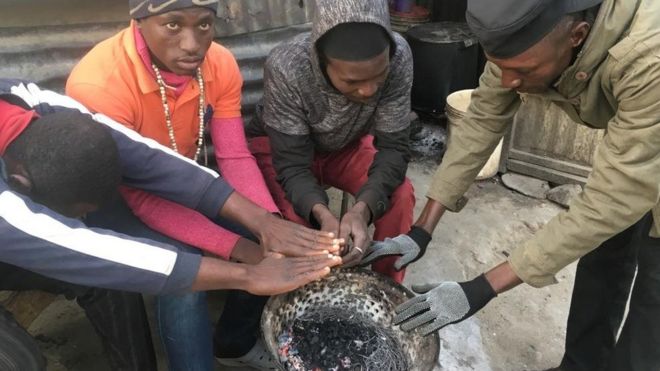 Some group of young men dey warm dia hands for fire.