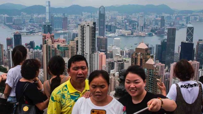 Turistas en Victoria Peak en Hong Kong posan para selfies y admiran la vista del puerto Victoria