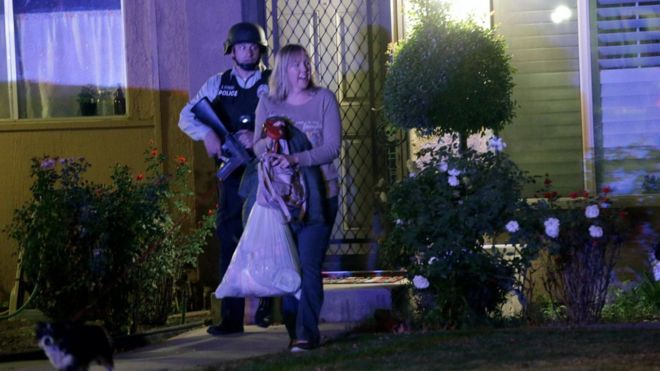 Полицейский сопровождает женщину из дома в среду, 2 декабря 2015 года, в Редлендсе, штат Калифорния.