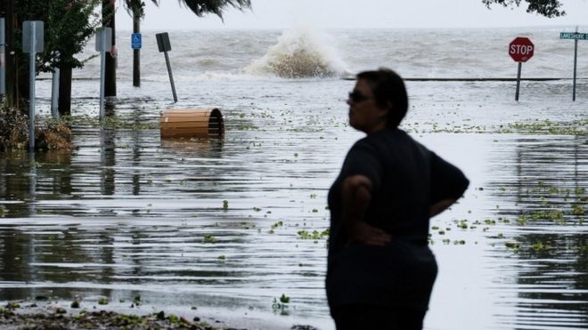 Женщина стоит перед затопленной дорогой возле озера Пончартрейн, когда приближается ураган Барри в Мандевилле, штат Луизиана