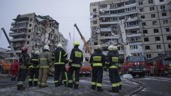 Firefighters stand near a residential building hit by a missile while their colleagues are conducting search and rescue operations on January 15, 2023 in Dnipro, Ukraine.