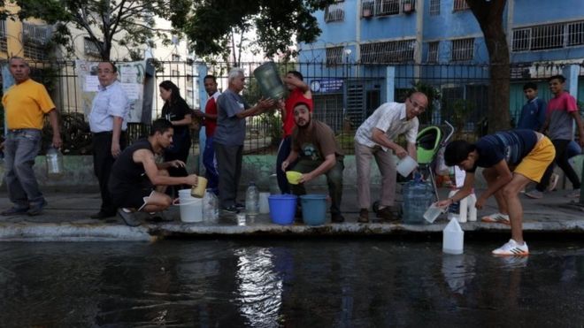 Группа людей пытается собрать воду в канализационной системе из-за нехватки воды из-за отключения электроэнергии в Каракасе, Венесуэла, 12 марта 2019 года. D
