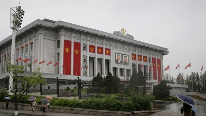 Северные корейцы проходят мимо правительственного здания, украшенного цветами и флагами правящей Рабочей партии (05 мая 2016 года)