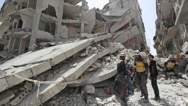 Спасатели гражданской обороны Сирии, также известные как Белые каски, ищут обломки разрушенного здания после взрыва в удерживаемом оппозицией городе Джиср-эш-Шугур (24 апреля 2019 года)