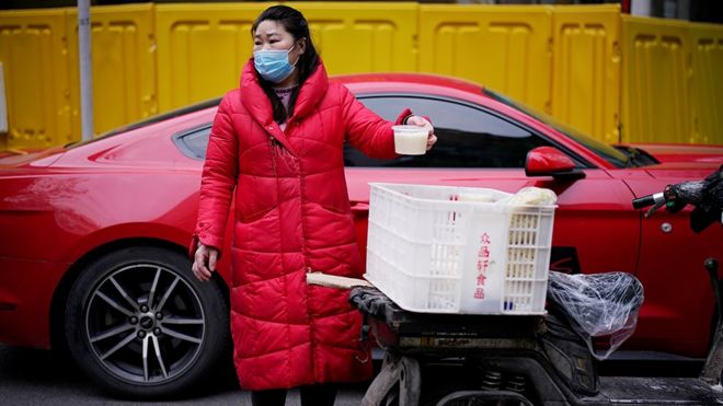 A vendor wearing a face mask sells a soup on a street