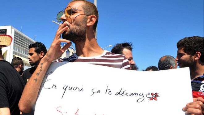 A Tunisian protester smokes a cigarette and holds a placard reading in French 'Why is it bothering you? If you fast and I eat?' during a demonstration for the right to eat and smoke in public during the Muslim dawn-to-dusk fasting month of Ramadan, on June 11, 2017,