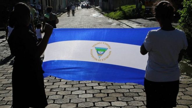 Dos mujeres sosteniendo una bandera de Nicaragua durante un funeral.