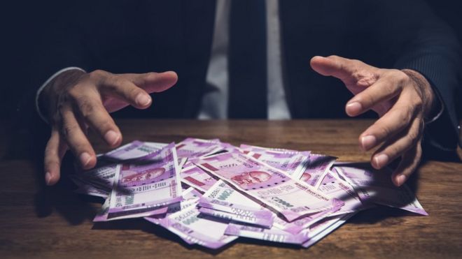 Businessman taking pile of money, Indian Rupee banknotes, on his desk in a dark office