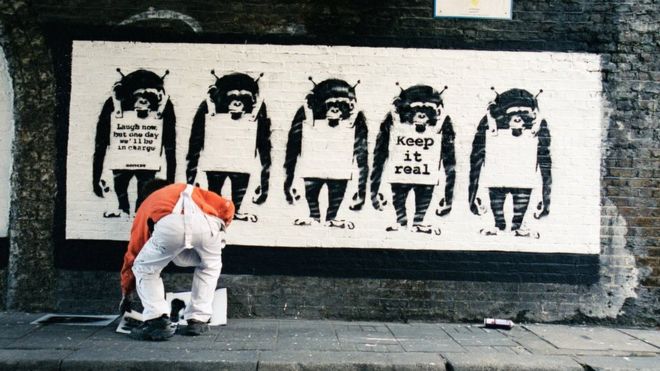 Artista ao lado de uma obra de Banksy