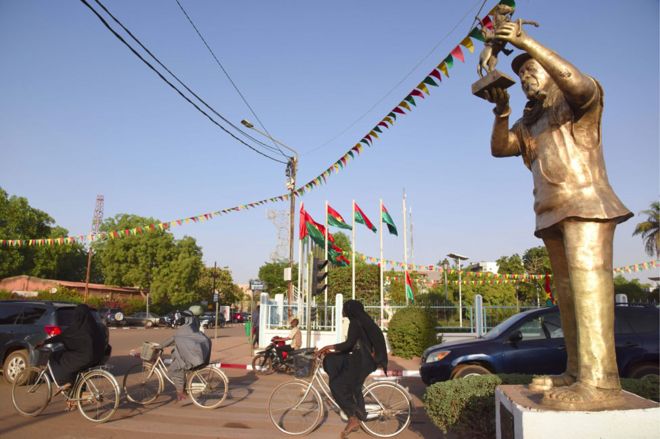 Люди проезжают мимо бронзовой статуи Сембене Усмане на улице столицы Буркина-Фасо Уагадугу 22 февраля 2019 года, в канун открытия Панафриканского фестиваля кино и телевидения (FESPACO)