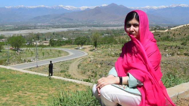 Malala Yousafzai, sentada em frente à paisagem de sua terra natal