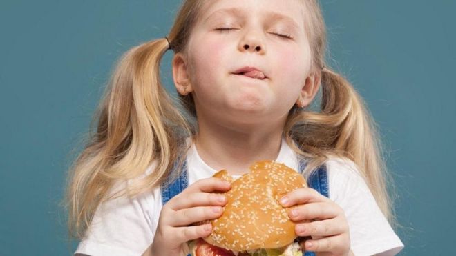Menina lambe a boca enquanto come hambúrguer