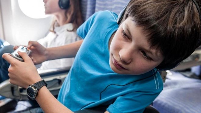 Un niño sentado en un asiento de avión, asomándose al pasillo