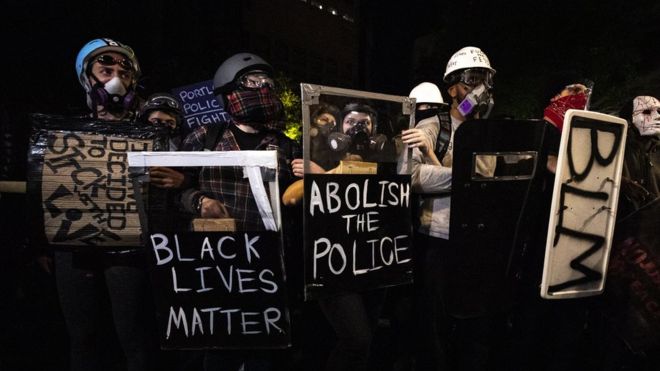 Протестующие в противогазах в Портленде держат плакаты Black Lives Matters