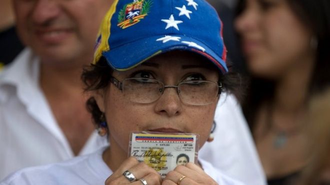 Женщина, держащая свои удостоверения личности, ждет в очереди, чтобы подписать петицию, чтобы инициировать референдум об отзыве президента Венесуэлы Николаса Мадуро в Сан-Кристобале, Венесуэла, среда, 27 апреля 2016 года.