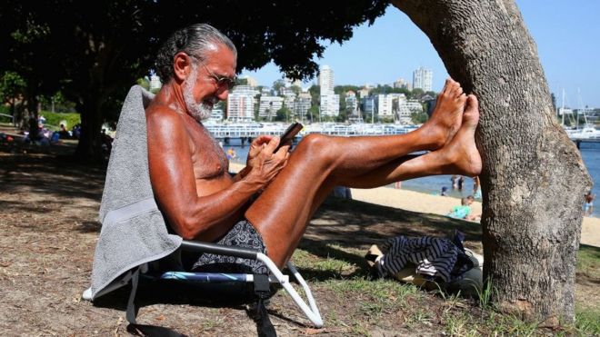 Пляжник читает свой телефон на солнце в Сиднее, январь 2019 года