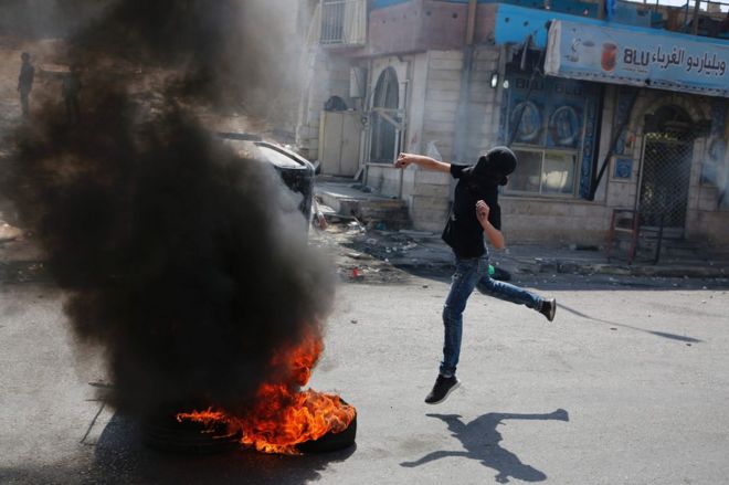 A masked Palestinian protester throws a stone at Israeli troops at the Qalandia checkpoint, 22 May