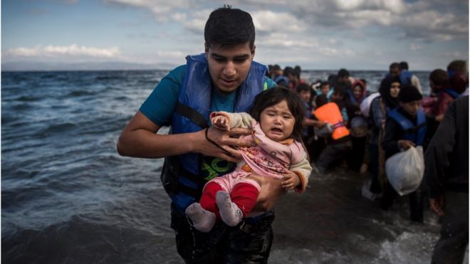 A man holding a baby disembarks from a dinghy after arriving from a Turkish coast to the northeastern Greek island of Lesbos, Sunday, Oct. 25, 2015.