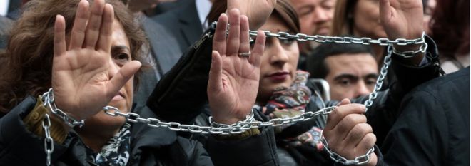 Журналисты с закованными руками протестуют против заключения в тюрьму главного редактора оппозиционной газеты Cumhuriyet Джана Дундара и представителя Анкары Эрдема Гюля