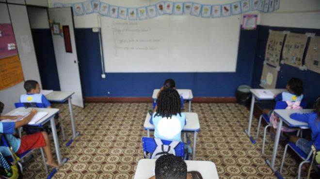 Crianças sentadas enfileiradas em cadeiras em sala de aula