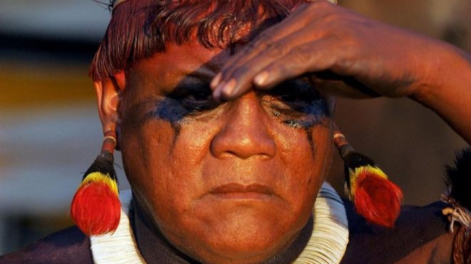 Close no rosto do líder indígena Aritana, que leva as mãos à testa para cobrir os olhos
