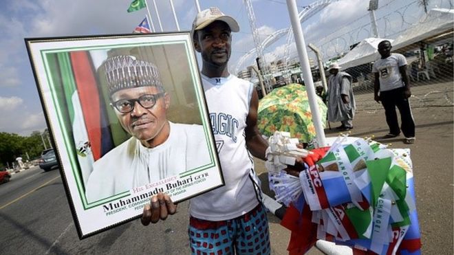 Поставщик продает партийные флаги Всесоюзного конгресса (APC) и фотографию в рамке избранного президента Мохаммаду Бухари перед завтрашней церемонией передачи в Абудже 28 мая 2015 года