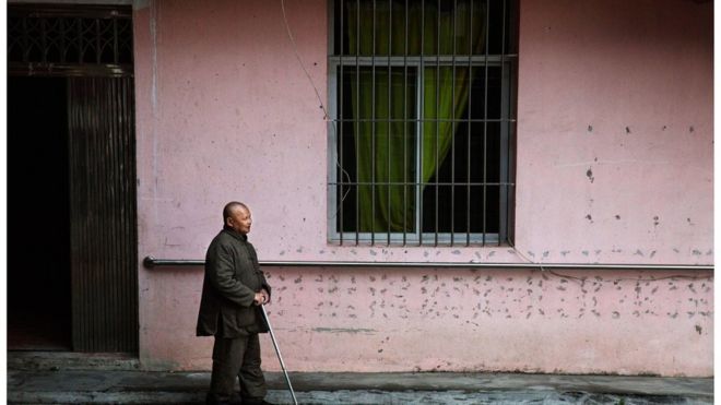 Пожилой слепой китаец проходит мимо здания