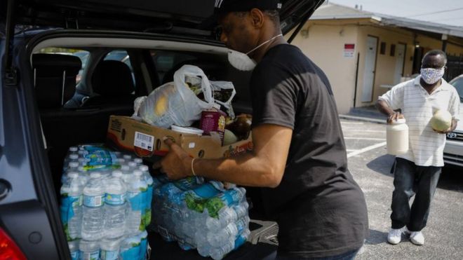 Un hombre llena su maletero de agua y alimentos
