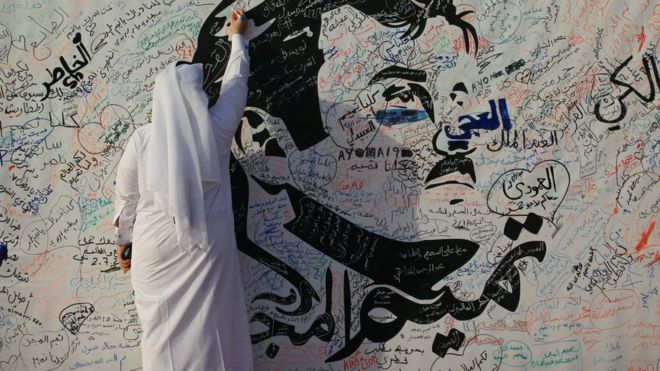 Мужчина пишет на картине, изображающей эмира Катара шейха Тамима бен Хамада Аль Тани в Дохе, Катар (2 июля 2017 года)