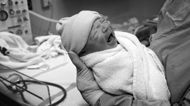 Ребенка держат акушеркой после рождения в родильном отделении NHS в Манчестере, Англия